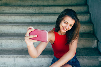 Portrait of smiling young woman using mobile phone while sitting on staircase