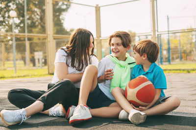 Cheerful high school students sit on the basketball court, relax after the game, talk and laugh.