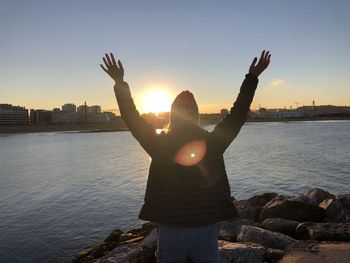 Rear view of woman standing by sea against sky during sunset