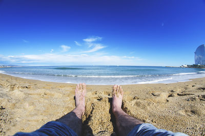 Low section of man sitting at beach against sky