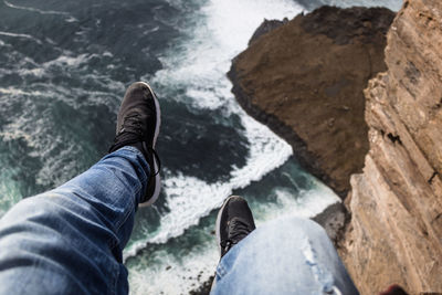 Low section of man sitting on rock formation over sea