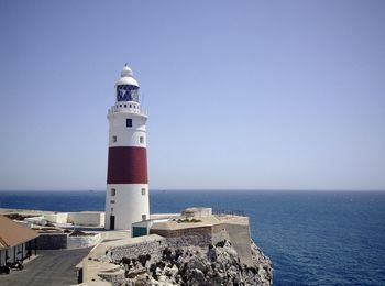 Lighthouse by sea against buildings against clear sky