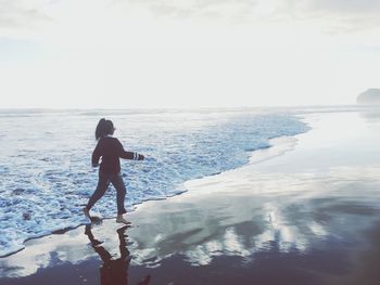 Woman walking away from surf reaching at beach