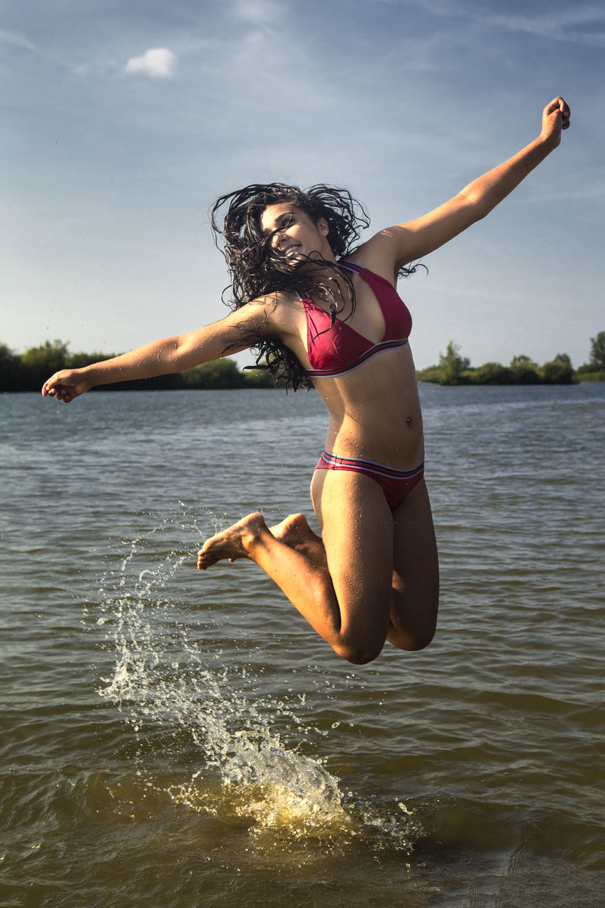 Full length of teenage girl wearing bikini jumping in lake