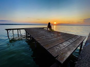 Woman sitting down on a wooden pontoon over the lake and enjoying the sunset