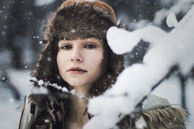 Portrait of woman by snowy branch during snowfall