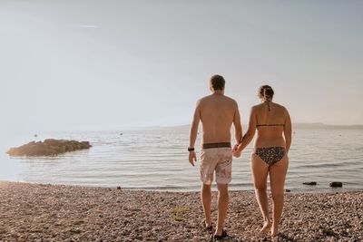 Rear view of couple standing on lakeshore against sky