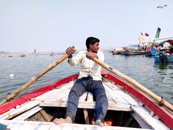 Young man sitting on boat against sky