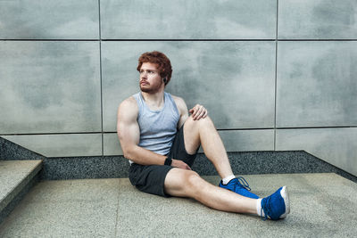 Young man looking away while sitting on floor