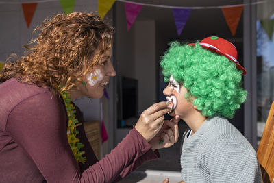 Mother painting her son's face like a clown