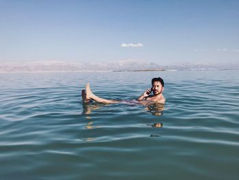 Portrait of shirtless man talking on mobile phone while swimming in infinity pool