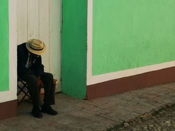 Full length of man sitting on footpath against wall