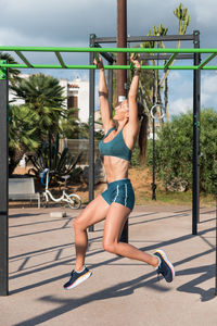 Side view of happy strong sportswoman in activewear exercising on monkey bars during workout on sunny day