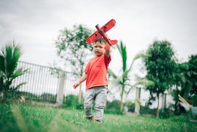 Full length of boy with arms raised against sky