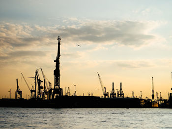 Cranes at commercial dock against sky during sunset