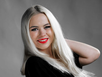 Portrait of smiling young woman wearing hat sitting against gray background