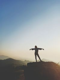 Silhouette woman with arms outstretched standing on mountain against clear sky