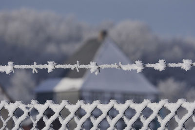 Close-up of snow covered fence and barb wire against house