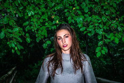 Portrait of beautiful young woman standing against trees