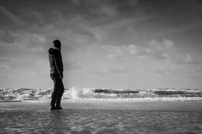 Rear view of man standing at sea shore against sky