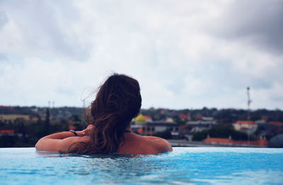 Rear view of woman swimming in infinity pool against sky