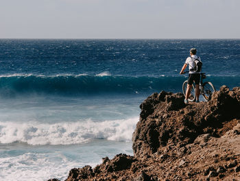 Man with bike on rock by sea against sky