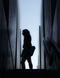 Side view of silhouette woman standing on staircase amidst buildings