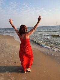 Rear view of woman with arms raised standing at beach