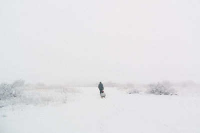 Man walking on snow field against clear sky
