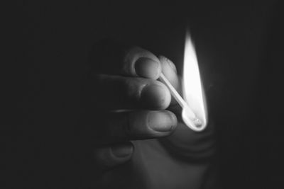 Cropped image of hand holding burning matchstick in darkroom
