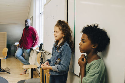 Male and female students standing against whiteboard at elementary school