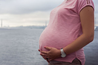 Midsection of pregnant woman standing against sea