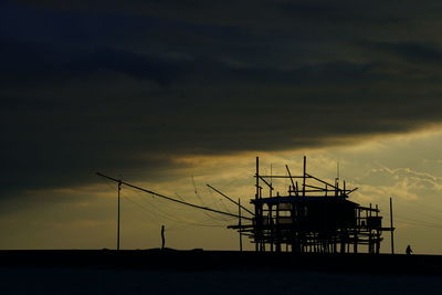 Silhouette stilt houses against cloudy sky at dusk