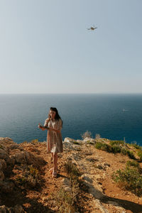 A young girl films herself with a drone near the sea.