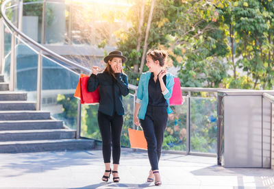 Portrait of happy young woman with friend holding shopping bags elevated walkway