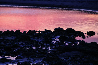 Silhouette rocks on beach against sky during sunset