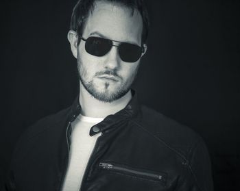 Portrait of confident young man in sunglasses standing against black background