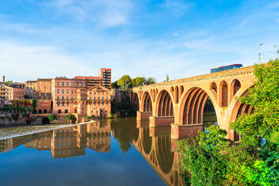 Arch bridge over river by buildings against sky