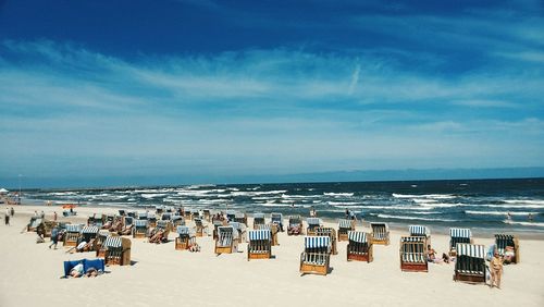 People relaxing on hooded beach chairs against blue cloudy sky