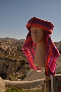 Woman wearing hat looking at rock against clear sky