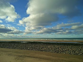 Scenic view of beach against cloudy sky