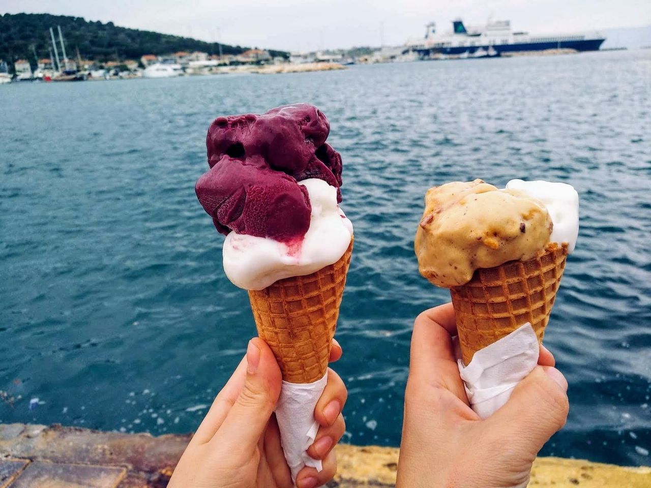 ice cream, human hand, sweet food, sweet, frozen food, hand, frozen, holding, ice cream cone, dairy product, human body part, cone, real people, water, dessert, focus on foreground, food and drink, food, indulgence, freshness, temptation, finger, outdoors, human limb