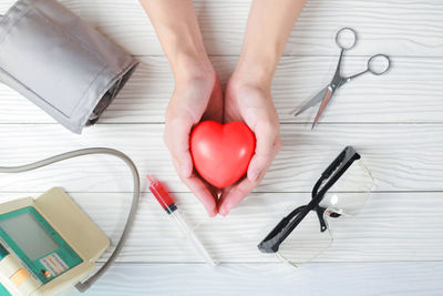 Cropped hands of doctor holding heart shape over table