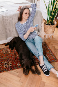 Full length of woman sitting on wooden floor with dog at home