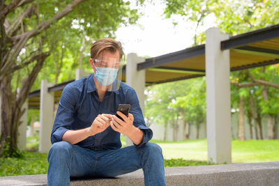 Young man using mobile phone sitting outdoors