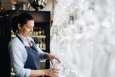 Smiling woman arranging wineglasses in restaurant