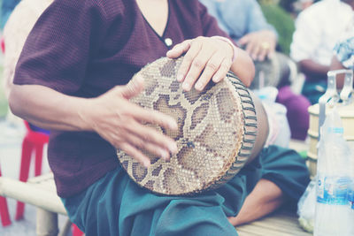 Midsection of woman playing drum while sitting outdoors