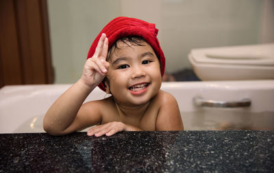 Portrait of cute baby girl showing peace sign in bathtub at home