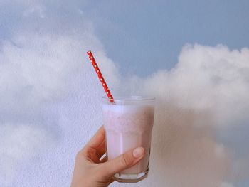 Cropped image of hand holding drink against mural wall