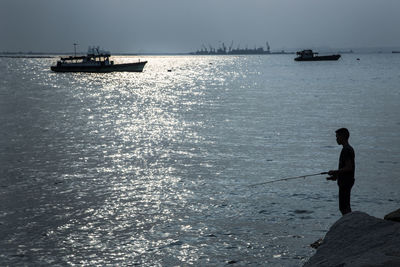 Man fishing in sea against sky